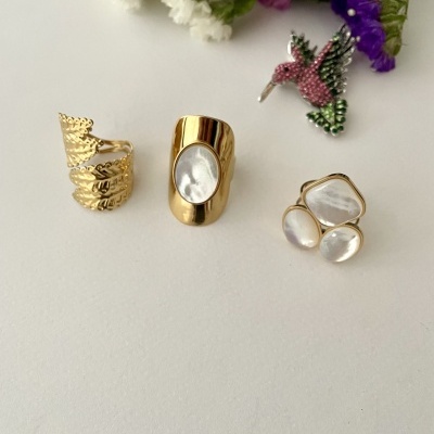 Três anéis dourados com pedras brancas e flores coloridas ao fundo