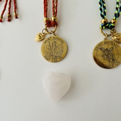 Colares com medalhões de santos e cordões trançados coloridos com um coração de pedra branca