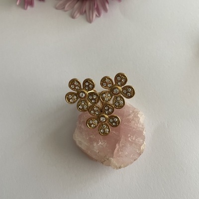 Anel dourado floral com pedras sobre cristal rosa e flores ao fundo