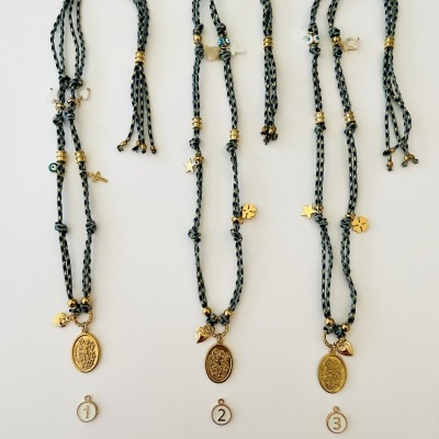 Três colares trançados em cinza e preto com pendentes dourados e etiquetas numeradas