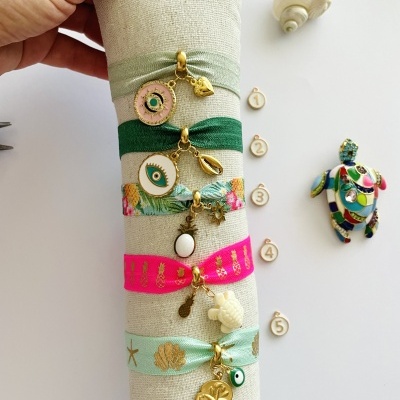 Pulseiras de tecido coloridas com pendentes dourados em suporte branco