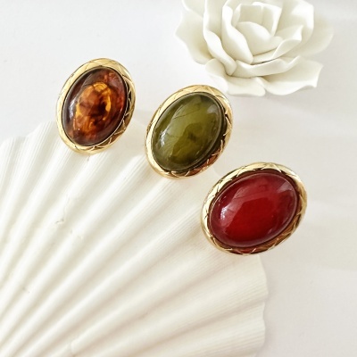 Três anéis com pedras coloridas em molduras douradas sobre concha branca