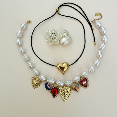 Conjunto de colares com pérolas e pendentes de corações coloridos e dourados, cordão preto com coração dourado, e dois anéis em forma de flor branca e concha.