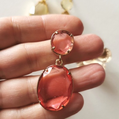 brinco pendente com pedras cor de rosa e estrutura dourada segurado por mão