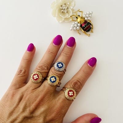 Mão feminina com quatro anéis dourados coloridos e broche de abelha com pérolas sobre fundo branco