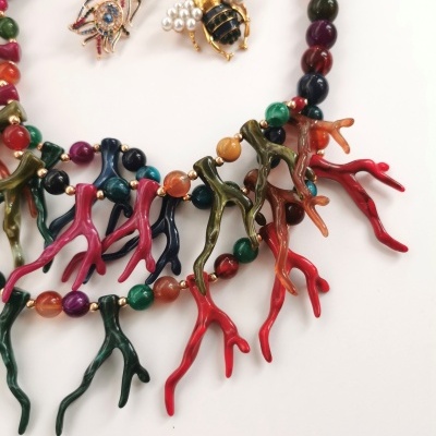 Colar com contas coloridas e ramos pendentes e dois broches dourados, uma folha e uma abelha, fundo branco