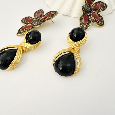 Brincos com design de flor em metal dourado e pedras vermelhas e pretas, com acabamento dourado e fundo branco.