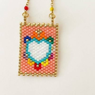 Colar com pendente retangular de contas coloridas com coração branco ao centro e corrente dourada com contas coloridas.