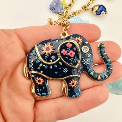 Colar com pingente de elefante azul com flores e detalhes dourados numa mão