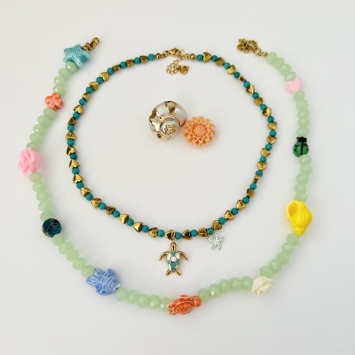 Duas pulseiras coloridas com contas e pendentes, concha branca e flor laranja em fundo branco.