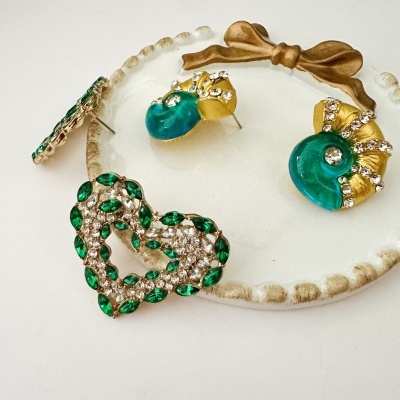 Brincos em dourado, verde e azul com pedras brilhantes sobre prato decorativo