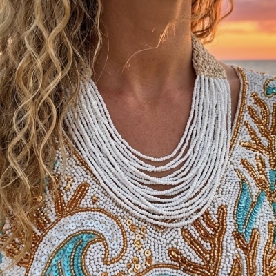 Colar de contas brancas com roupa bordada colorida e cabelo loiro ondulado