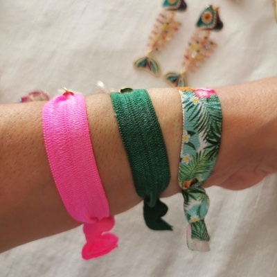 Três pulseiras de tecido coloridas no pulso sobre fundo branco.