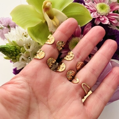 Pequenas peças metálicas douradas na mão diante de flores variadas.