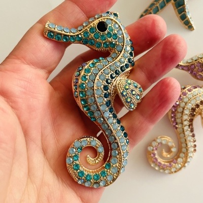 Broche cavalo-marinho dourado com pedras azuis na mão