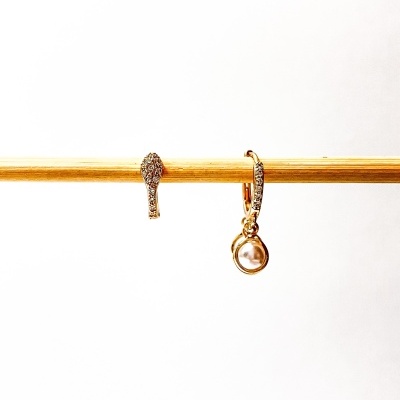 Brincos dourados com cristais e pérola pendurados em barra de madeira