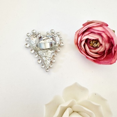Anel de metal prateado em base de coração com flores artificiais rosa e branca