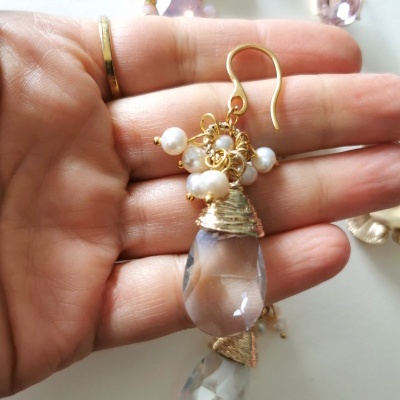 Brinco pendente dourado com pérolas e gotas facetadas numa mão