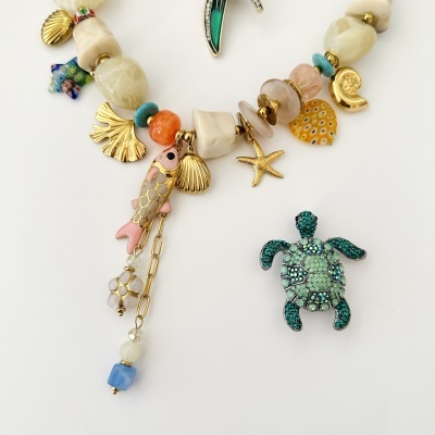 Colar com pingentes coloridos e broche de tartaruga verde brilhante sobre fundo branco.