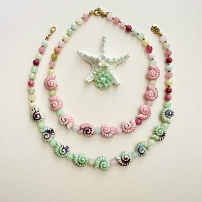 Dois colares coloridos com contas em espiral e fechos dourados, junto a estrela do mar e suculenta verde
