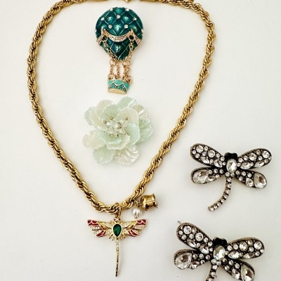 Bijuteria com colar, broche e brincos decorativos em fundo branco.