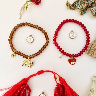 Pulseiras de contas castanha e vermelha com pendentes e medalhões numerados, decoradas com flores e franjas.