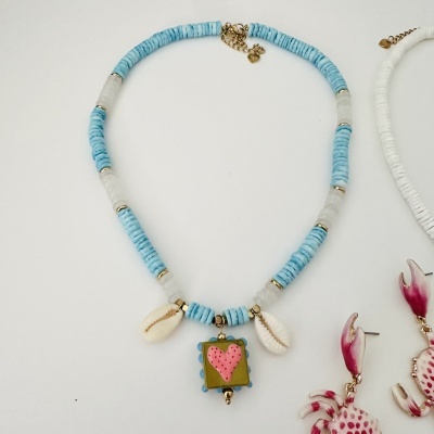 Colar azul e transparente com pendente de coração e búzios, junto de brincos rosas e brancos