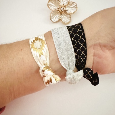 Conjunto de três pulseiras elásticas coloridas com padrões e nó, usadas num pulso