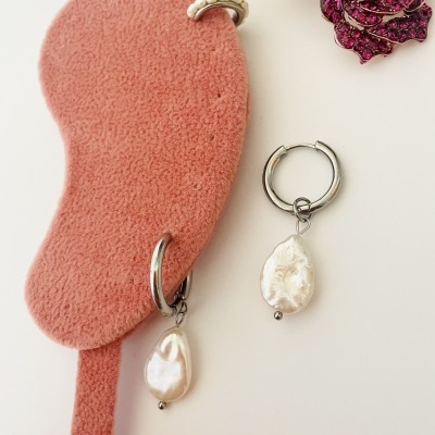 Brincos de pérola em argolas prateadas sobre suporte de veludo rosa com broche de flores decorativo