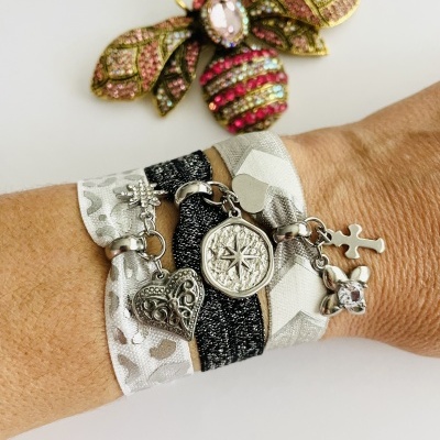 Pulseira de tecido cinza com pendentes metálicos prateados e broche de abelha colorida ao fundo