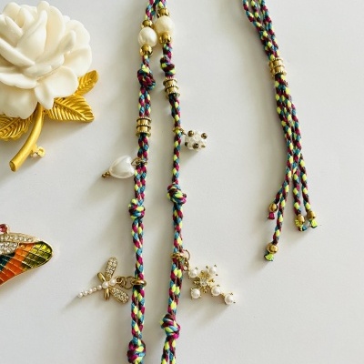 Colar colorido trançado com pérolas e contas sobre superfície branca com broches decorativos