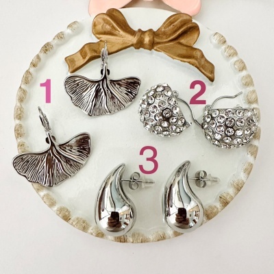 Três pares de brincos em prato branco com laço castanho, numerados de 1 a 3.