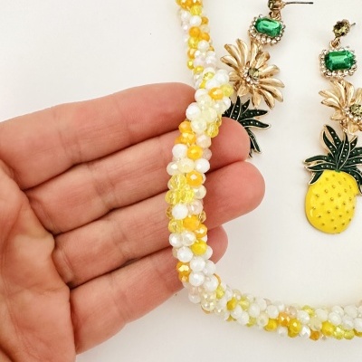 Colar de pérolas coloridas com brincos de abacaxi e folhas verdes num fundo branco