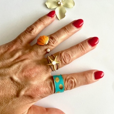 mão com anéis variados coloridos sobre fundo branco com flor decorativa