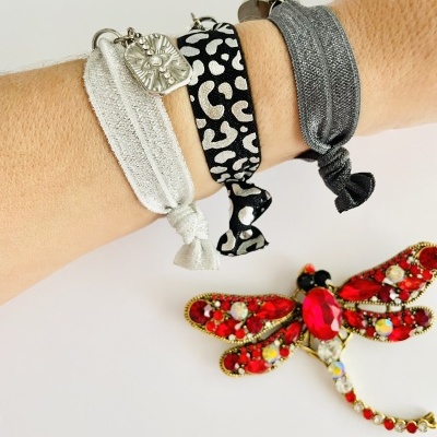 Três pulseiras em tecido com padrão diferente e um broche de libélula colorido ao lado