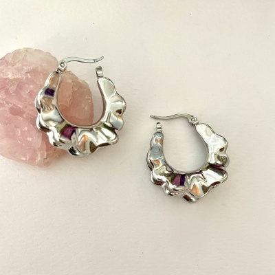 Brincos de argola prateados ondulados sobre superfície branca com pedra rosa