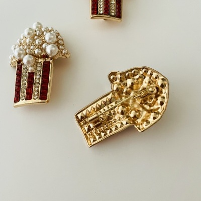 Broches dourados em forma de pipoca com pérolas e pedras vermelhas
