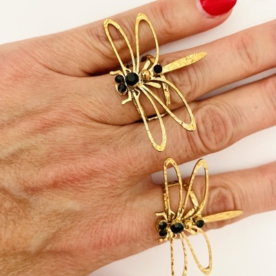 Anel dourado de libélula com pedras pretas em dedos femininos sobre fundo branco