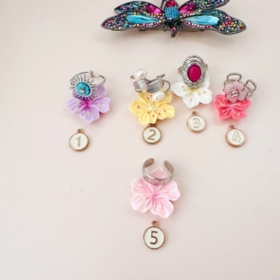 Anéis com flores de tecido em várias cores e etiquetas numéricas, com broche de libélula colorido acima