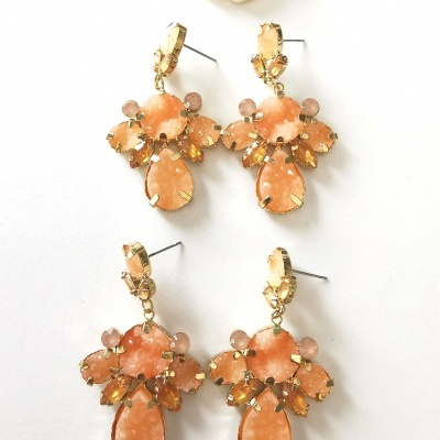 Dois pares de brincos dourados com pedras cor de pêssego e uma flor branca decorativa