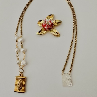 Colar dourado com corrente dupla e broche em forma de flor dourada.