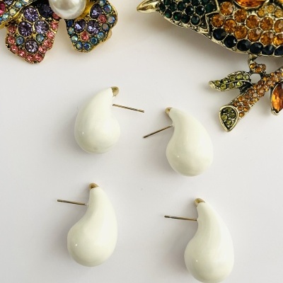 Dois pares de brincos brancos em forma de gota junto a broches coloridos sobre fundo branco
