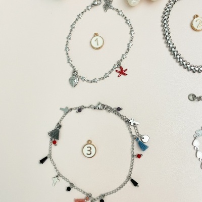 Duas pulseiras prateadas com pendentes variados e conchas decorativas sobre fundo claro