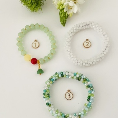 Três pulseiras coloridas numeradas sobre fundo branco com flores