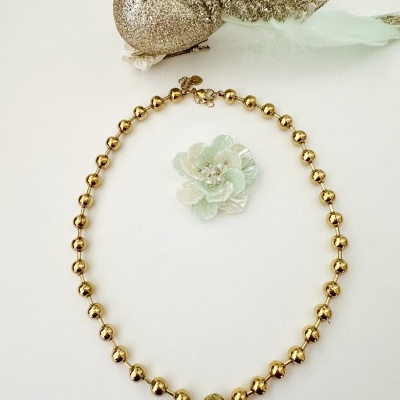 Colar de contas douradas com broche de flor verde claro em fundo branco
