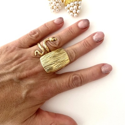 Mão com anel dourado em forma de cobra e brincos dourados com pérolas