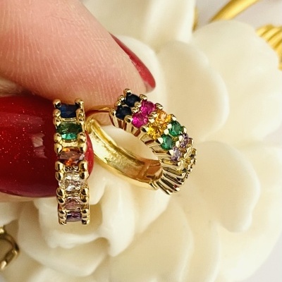 Brincos de argola dourados com pedras coloridas sobre flor branca decorativa