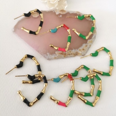 Brincos de argola dourados em forma de bambu com detalhes coloridos, sobre pedra rosa e flor branca