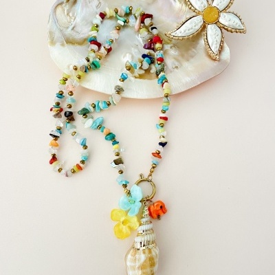 Colar colorido com contas variadas e pendente decorativo sobre bolsa acetinada com aplique de flor