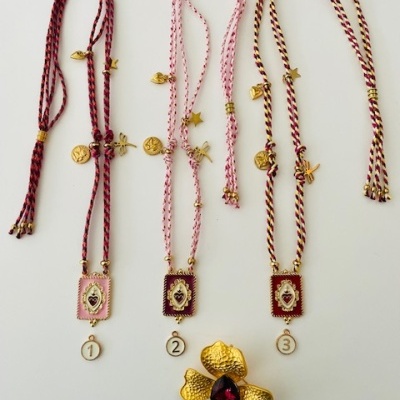 Três colares trançados coloridos com pingentes dourados e broche dourado em formato de flor